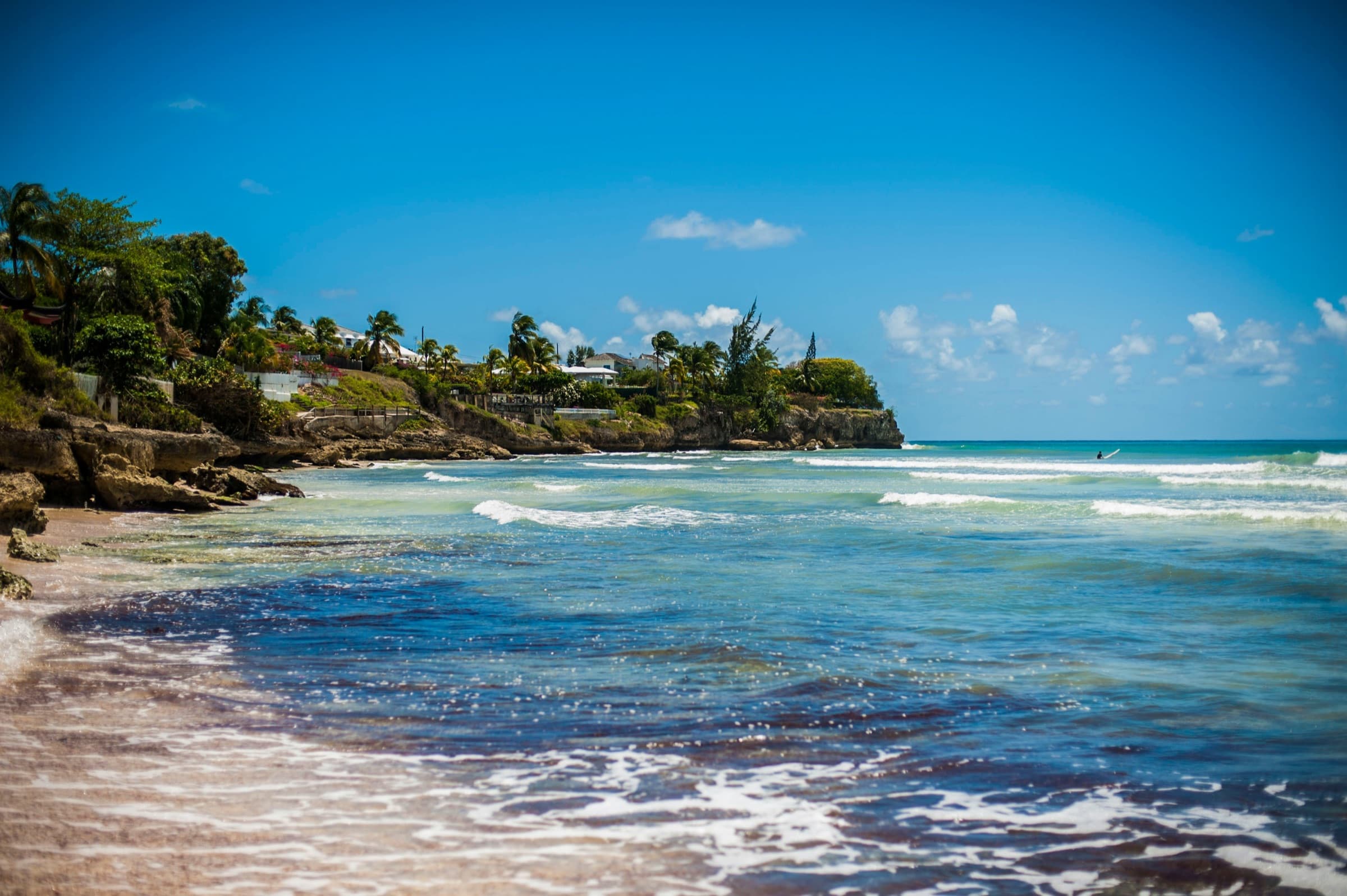 Turquoise waves rolling onto a sandy beach below a palm-covered headland under a blue sky